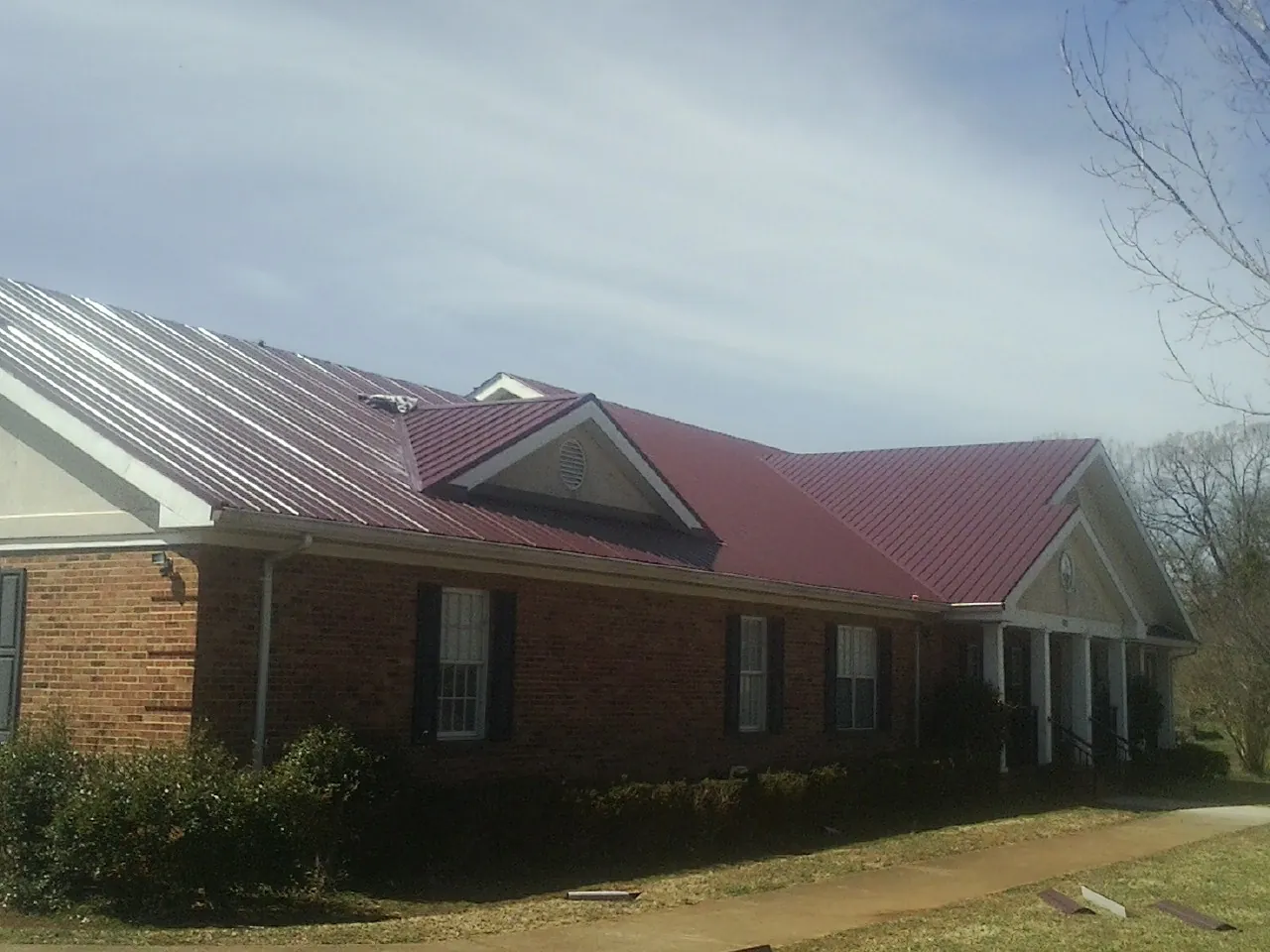 Red metal roof with gabled entries on a long brick building, from a Hail Damage Roof Repair job in Warrenville