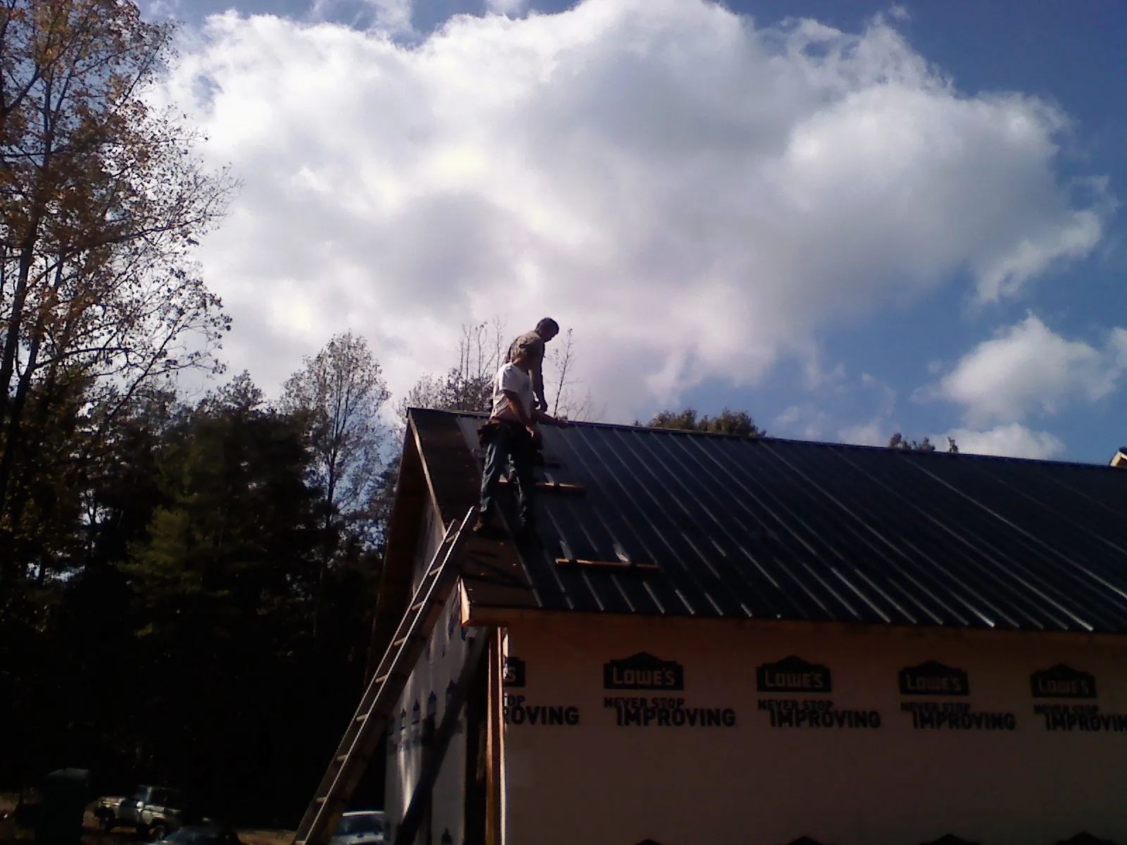 Roofer fastening dark metal panels high against a cloudy sky, from a Roof Inspection job in Warrenville